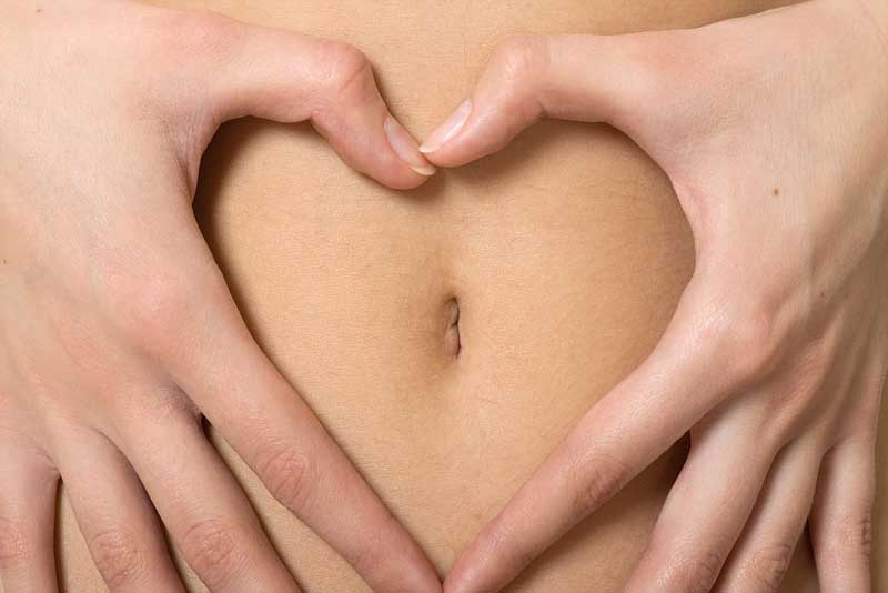 Woman's tummy with the hands forming a heart around the belly button